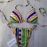 COSTUME DONNA ME FUI A DUE PEZZI DELLA STAGIONE ESTATE 2026. TRIANGOLO CON IMBOTTITURA ESTRAIBILE E DETTAGLIO IN METALLO COLOR ORO TRA LE COPPE. BASE PANNA CON FANTASIA VERDE E VIOLA